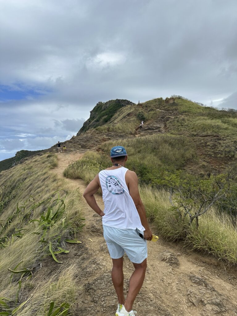 A hiker carefully climbing the steep and rocky path of the Lanikai Pillbox trail in Oahu.