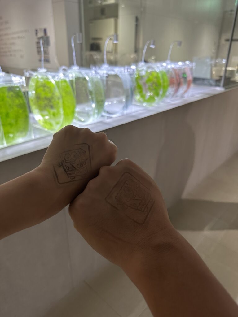 A person holding tickets in front of a modern industrial-style aquarium interior with a SpongeBob SquarePants character cutout in the background.