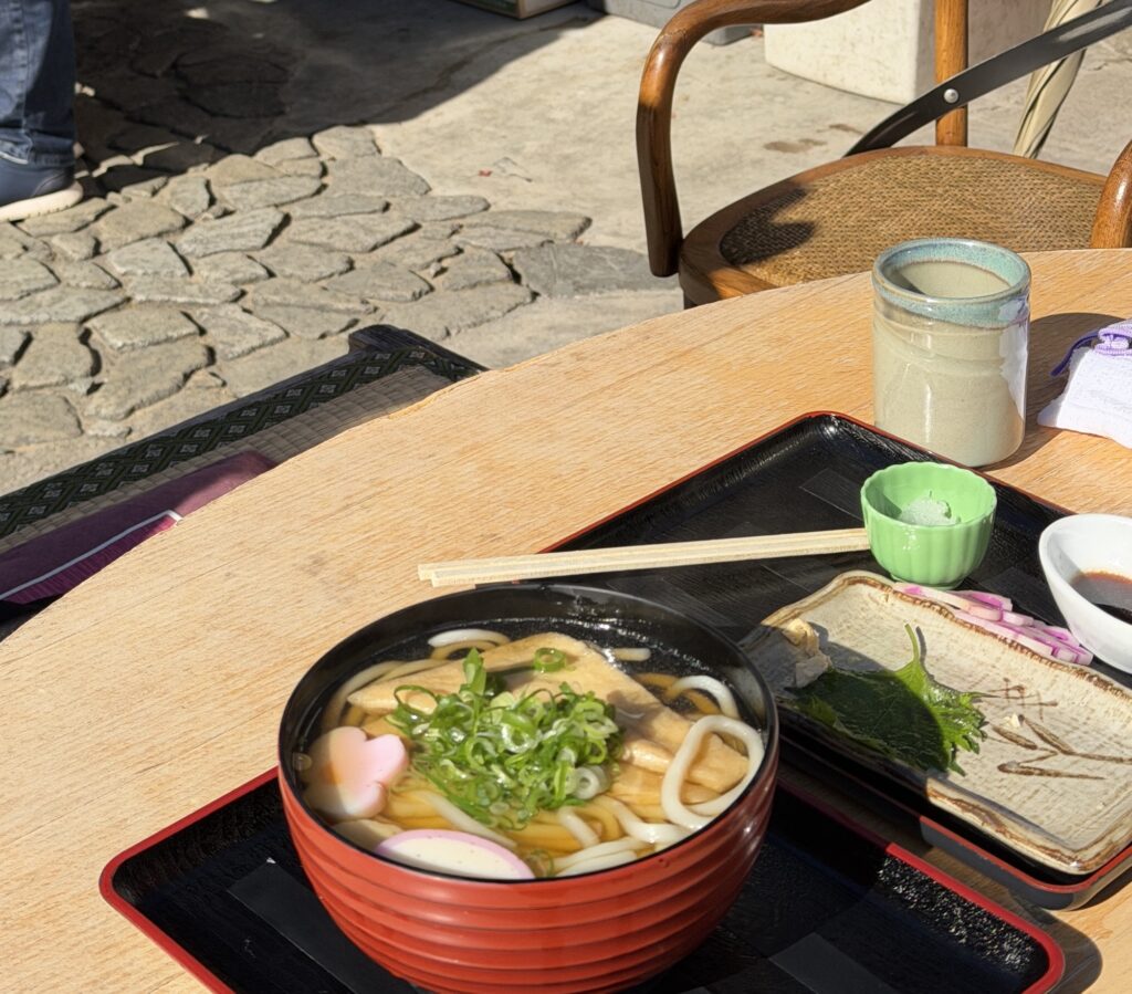 Hot bowl of Kitsune Udon with large fried tofu on a wooden table at an Arashiyama restaurant.